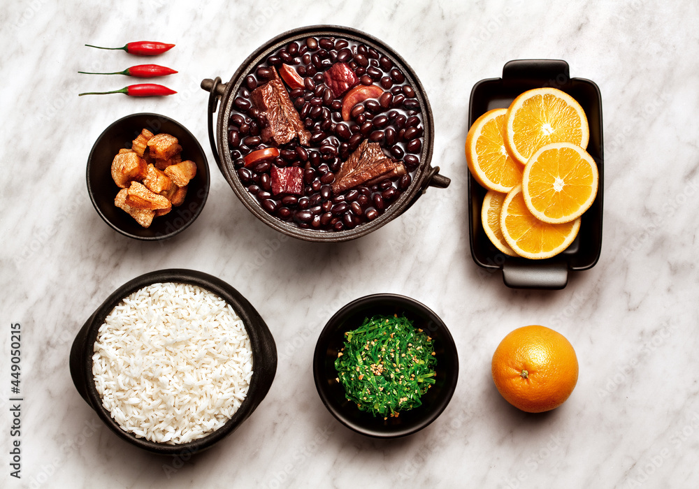 Ingredientes de feijoada sobre fundo de mármore - feijão, arroz, torresmo, couve, laranja e pimenta